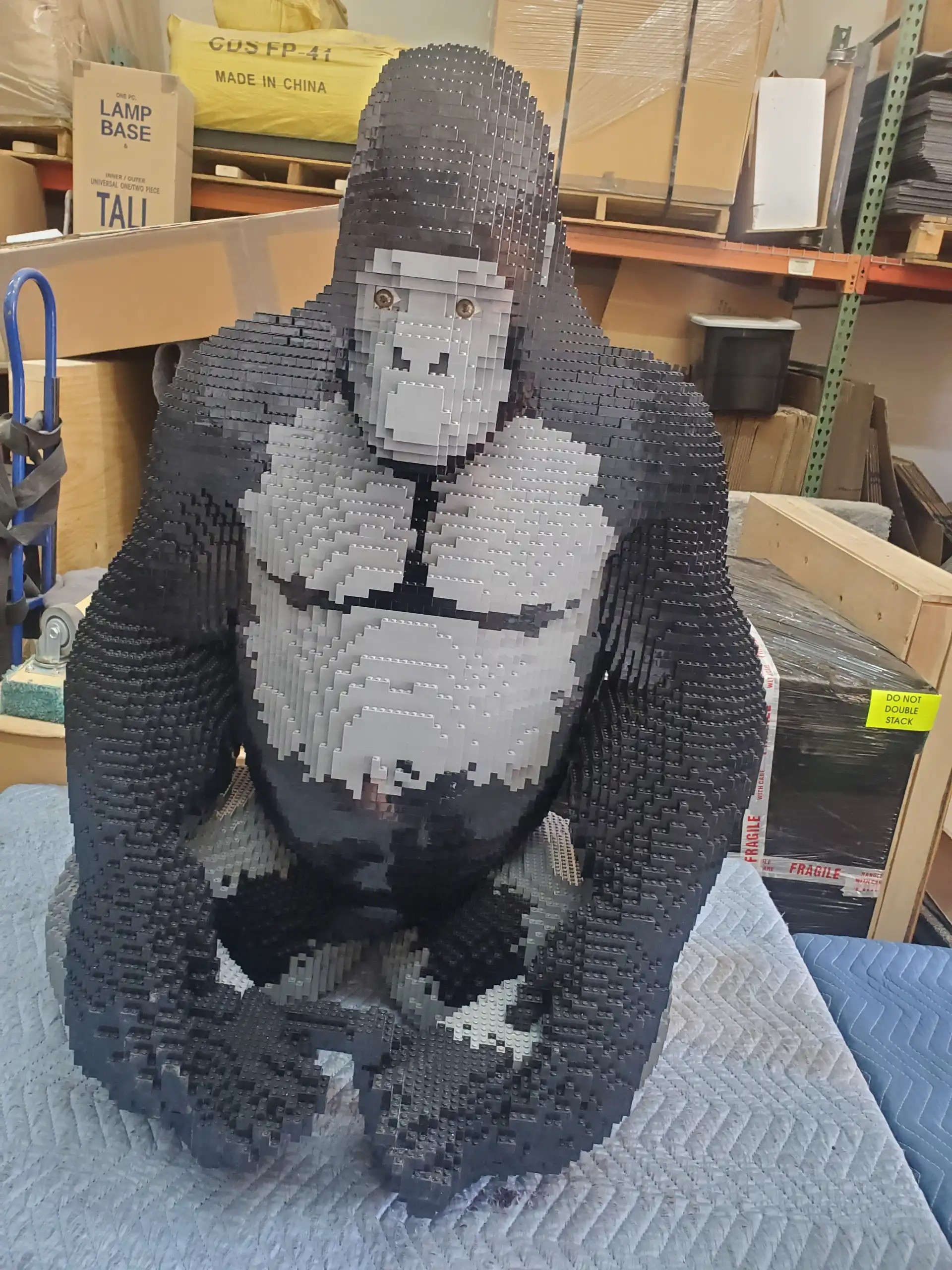 A large brick-built gorilla sculpture resting on padding in the warehouse