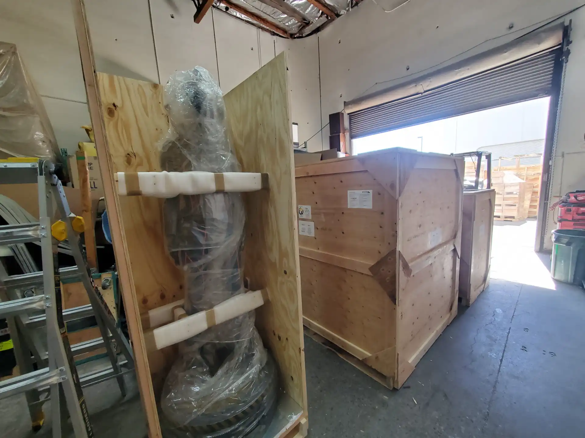 A tall wrapped sculpture braced in its crate beside sealed crates at the dock